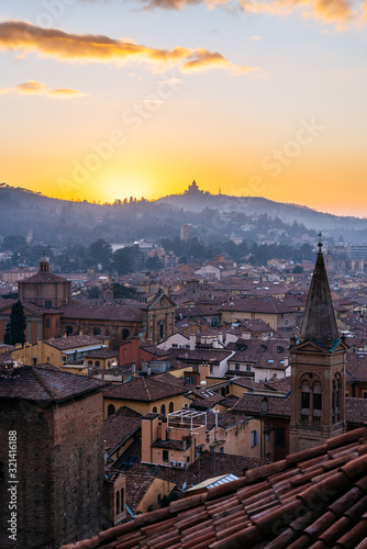 Sunset in Bologna, aerial view of rooftops and hill with San Luca Monastery.