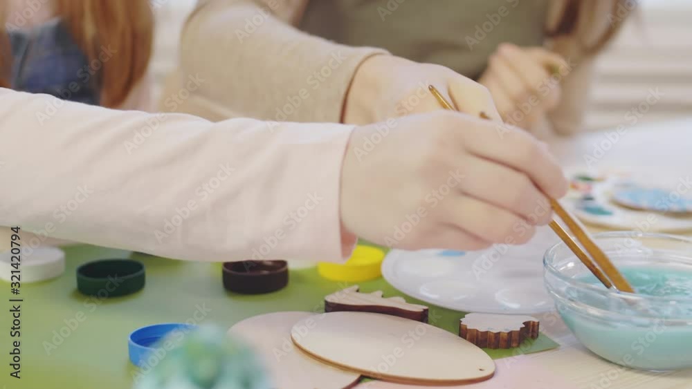 Close up shot of hands of unrecognizable woman and girl washing their brushes and painting on wooden ornament Close up shot of hands of unrecognizable woman and girl washing their brushes and painting on wooden ornament