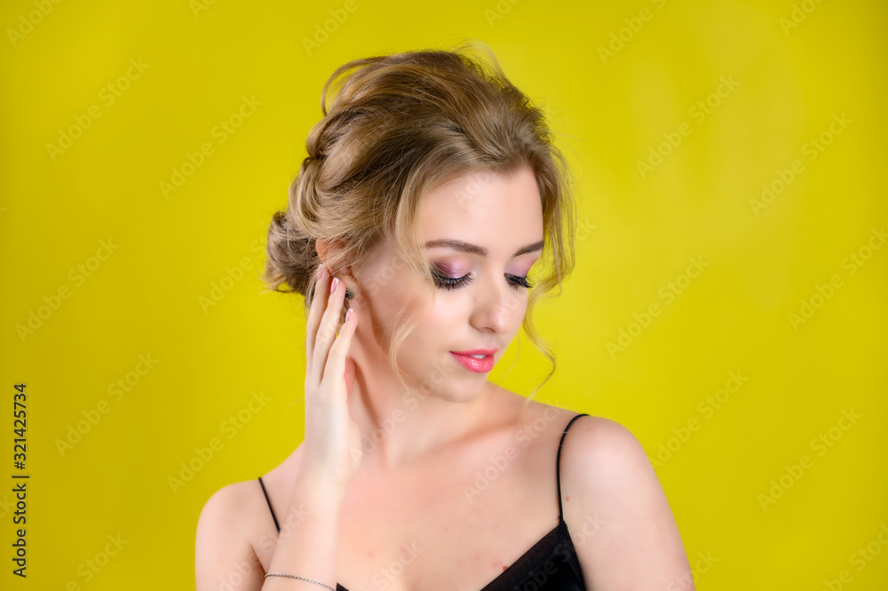The concept of cosmetics, fashion and style. Glamorous beauty portrait of a pretty blonde model with excellent makeup and a beautiful hairstyle on a yellow background in the studio.