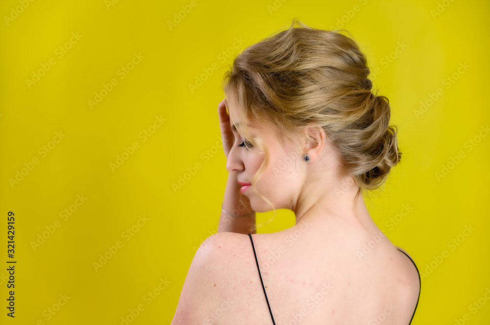 Obraz premium Glamorous beauty rear view portrait of a pretty blonde model with excellent make-up and beautiful hairstyle on a yellow background in the studio. The concept of cosmetics, fashion and style.