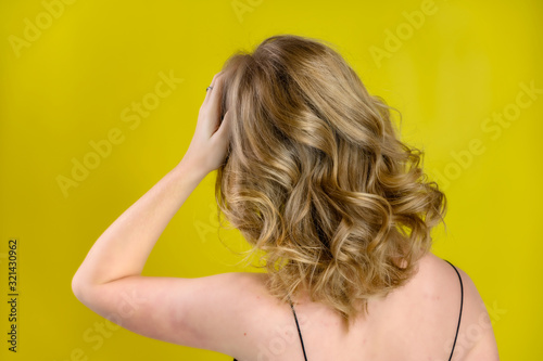 Glamorous beauty rear view portrait of a pretty model with blond hair with great makeup and a beautiful hairstyle on a yellow background in the studio. The concept of cosmetics, fashion and style.