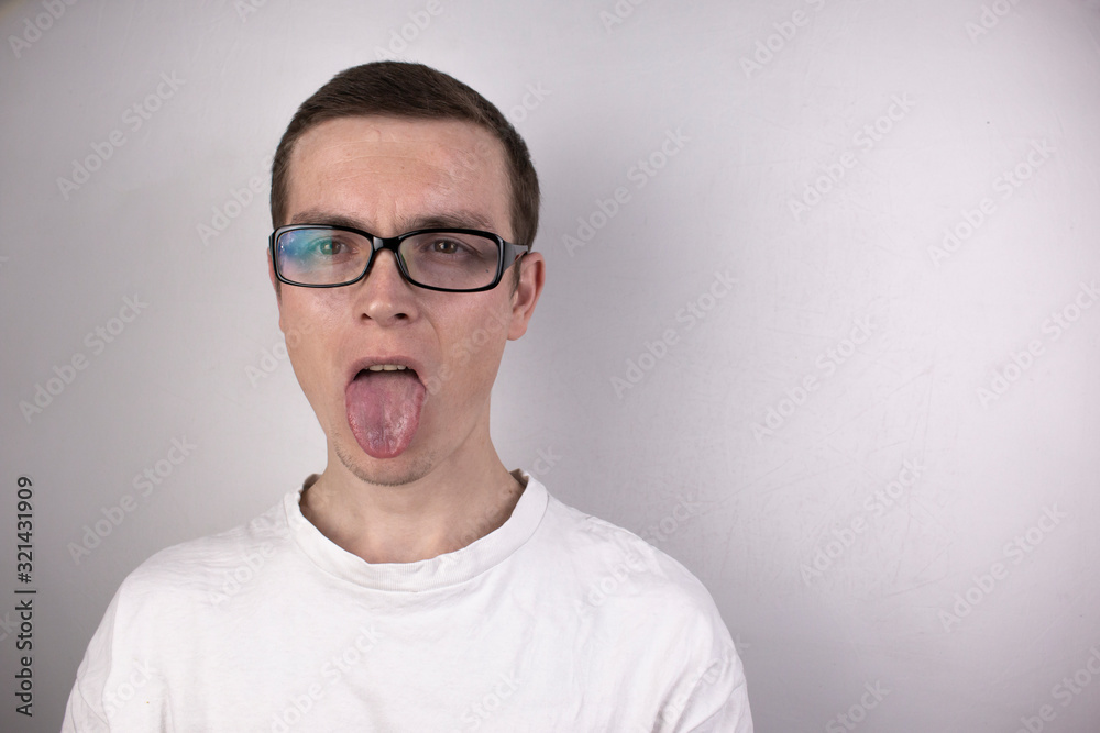 A guy in a white T-shirt on a gray background, wearing transparent glasses in a black frame, stuck his tongue out A guy in a white T-shirt on a gray background, wearing transparent glasses in a black frame, stuck his tongue out