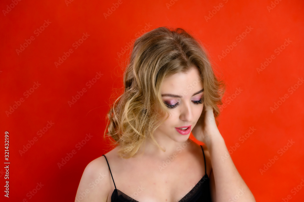 Glamorous beauty front view portrait of a pretty model with blond hair with great makeup and a beautiful hairstyle on a red background in the studio. The concept of cosmetics, fashion and style. Glamorous beauty front view portrait of a pretty model with blond hair with great makeup and a beautiful hairstyle on a red background in the studio. The concept of cosmetics, fashion and style.