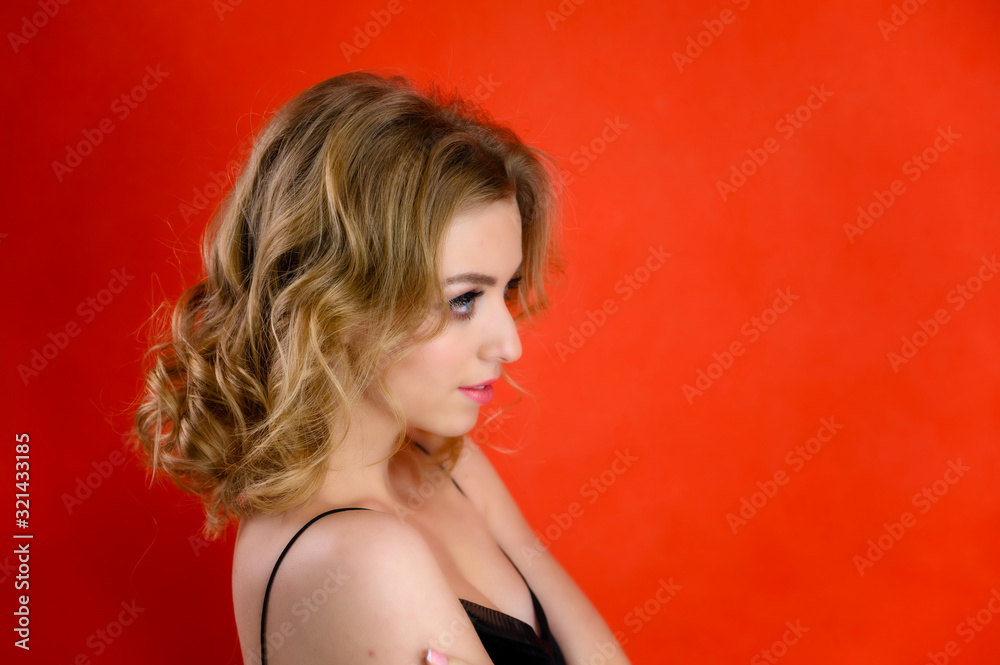 Glamorous beauty portrait side view of a pretty model with blond hair with great makeup and a beautiful hairstyle on a red background in the studio. The concept of cosmetics, fashion and style. Glamorous beauty portrait side view of a pretty model with blond hair with great makeup and a beautiful hairstyle on a red background in the studio. The concept of cosmetics, fashion and style.