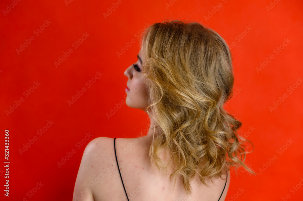 Glamorous beauty rear view portrait of a pretty model with blond hair with great makeup and a beautiful hairstyle on a red background in the studio. The concept of cosmetics, fashion and style. Glamorous beauty rear view portrait of a pretty model with blond hair with great makeup and a beautiful hairstyle on a red background in the studio. The concept of cosmetics, fashion and style.