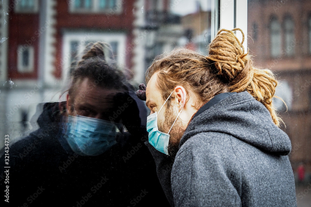 Handsome young European man in winter clothes on the street with a medical face mask on looking inside the pharmacy through the shop window Handsome young European man in winter clothes on the street with a medical face mask on looking inside the pharmacy through the shop window