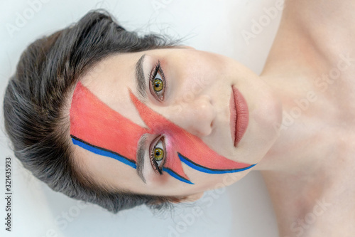 Fotografi Close-up portrait of a beautiful girl with creative make-up, who lies on the floor in the studio