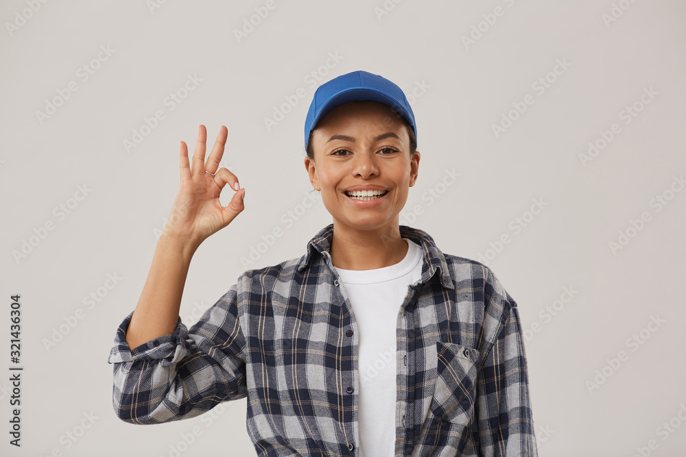 Waist up portrait of beautiful female worker showing OK sign and smiling at camera while standing against white background, copy space Waist up portrait of beautiful female worker showing OK sign and smiling at camera while standing against white background, copy space