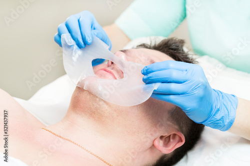 Cosmetic procedure for applying a therapeutic mask to a young man in a beauty salon.