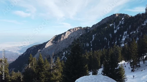 Snowy peaks and cliffs of the Postavaru mountain range in Romania , part of the Carpathian mountains , with snow covered ski slopes and skiers engaged in winter sports activities. photo