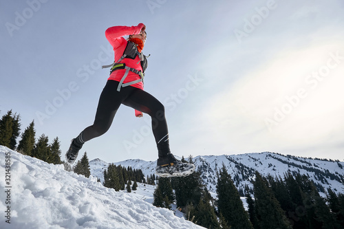 Trail runner woman running in winter mountains on snow. Dynamic running downhill on trail woman athlete runner side view