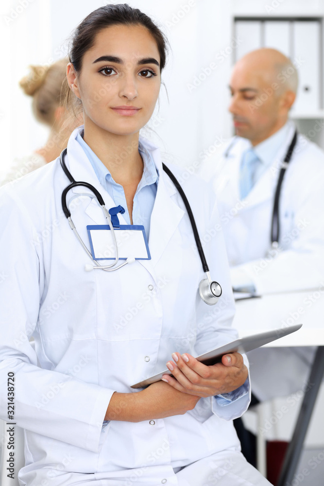 Doctor woman in clinic with colleagues at the background. Hispanic or latin american staff in medicine
