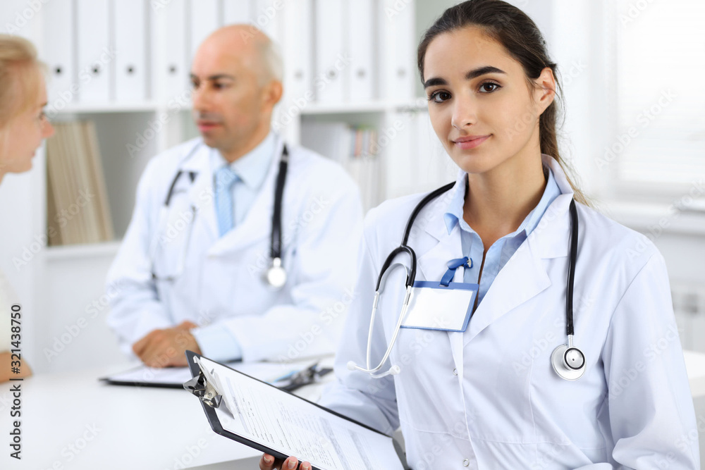 Doctor woman in clinic with colleagues at the background. Hispanic or latin american staff in medicine Doctor woman in clinic with colleagues at the background. Hispanic or latin american staff in medicine
