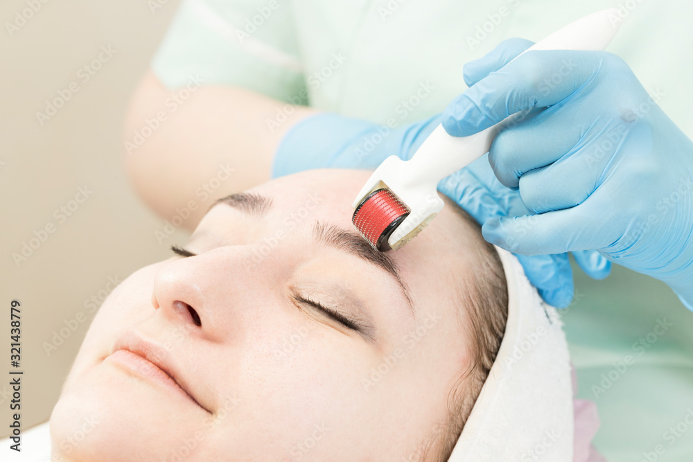 The woman undergoes the procedure of medical micro needle therapy with a modern medical instrument derma roller. The woman undergoes the procedure of medical micro needle therapy with a modern medical instrument derma roller.