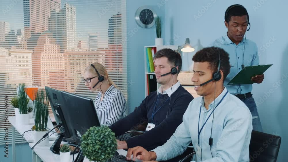 Multiethnic customer service representative telling his colleagues a joke while calling to the clients. They laughing and continuing working.