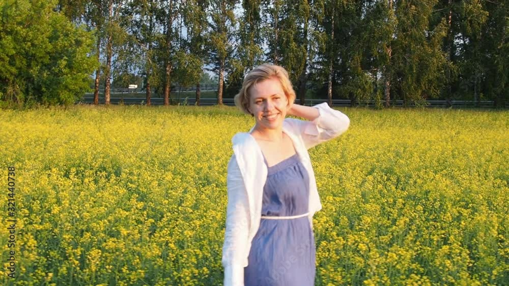 an attractive young blonde woman walks through a field of rapeseed, smiling and spinning merrily. Slow motion an attractive young blonde woman walks through a field of rapeseed, smiling and spinning merrily. Slow motion