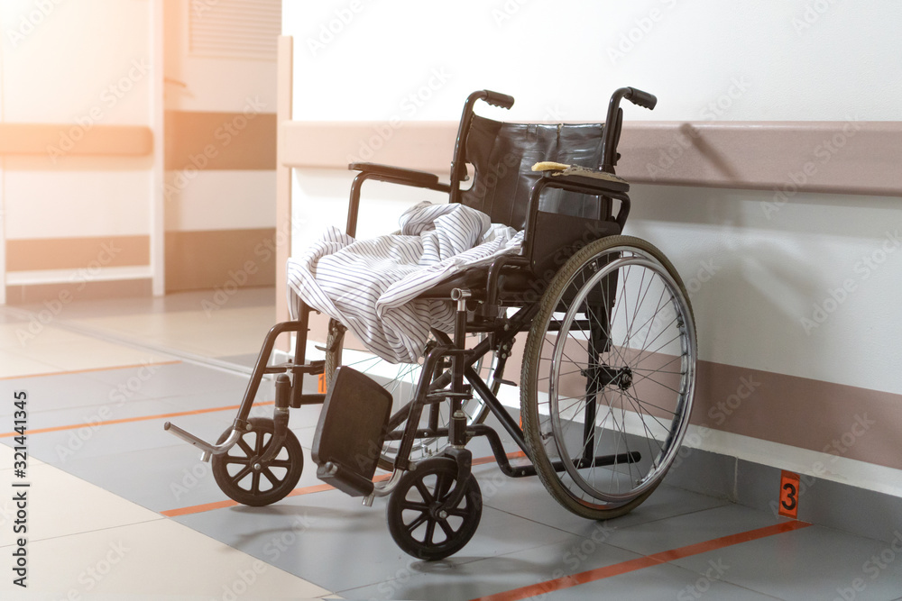 An old wheelchair in a hospital is parked. No people. The sun shines