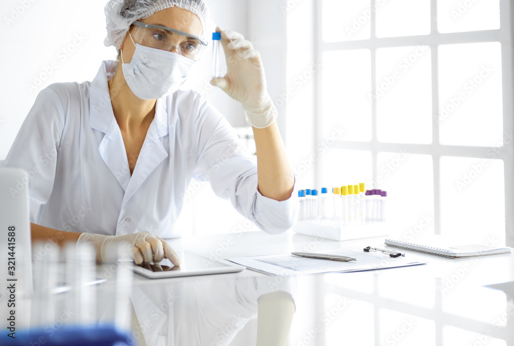 Professional female scientist in protective eyeglasses researching tube with reagents in laboratory. Concepts of medicine and research