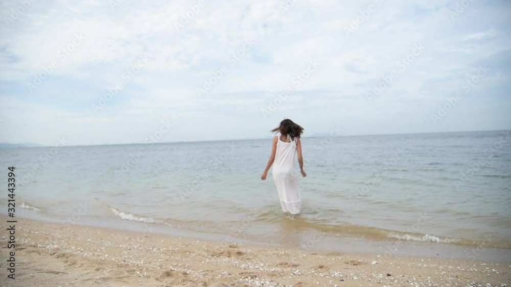 Cheerful asian woman barefoot walking on tropical summer beach. Woman walking along wave of sea water and sand on the beach. Enjoyment barefoot walk outdoor with freedom. Relaxation Travel Concept. Cheerful asian woman barefoot walking on tropical summer beach. Woman walking along wave of sea water and sand on the beach. Enjoyment barefoot walk outdoor with freedom. Relaxation Travel Concept.