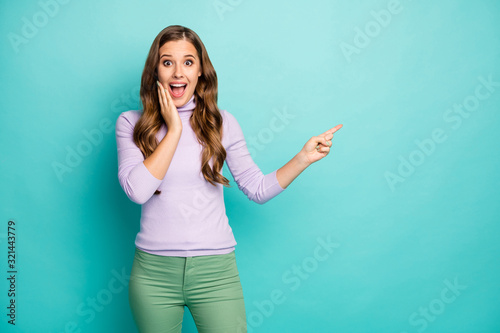 Photo of funky pretty lady open mouth indicate finger empty space advising novelty product discount price wear lilac jumper green trousers isolated teal pastel color background