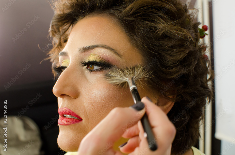 Make-up artist working with brush on model face. Side portrait of young woman in beauty studio interior. Close up of beautiful young brunette female model getting blush with big cosmetic brush Make-up artist working with brush on model face. Side portrait of young woman in beauty studio interior. Close up of beautiful young brunette female model getting blush with big cosmetic brush