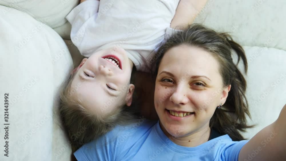 Young mother and child playing lying on the bed and taking a selfie Young mother and child playing lying on the bed and taking a selfie
