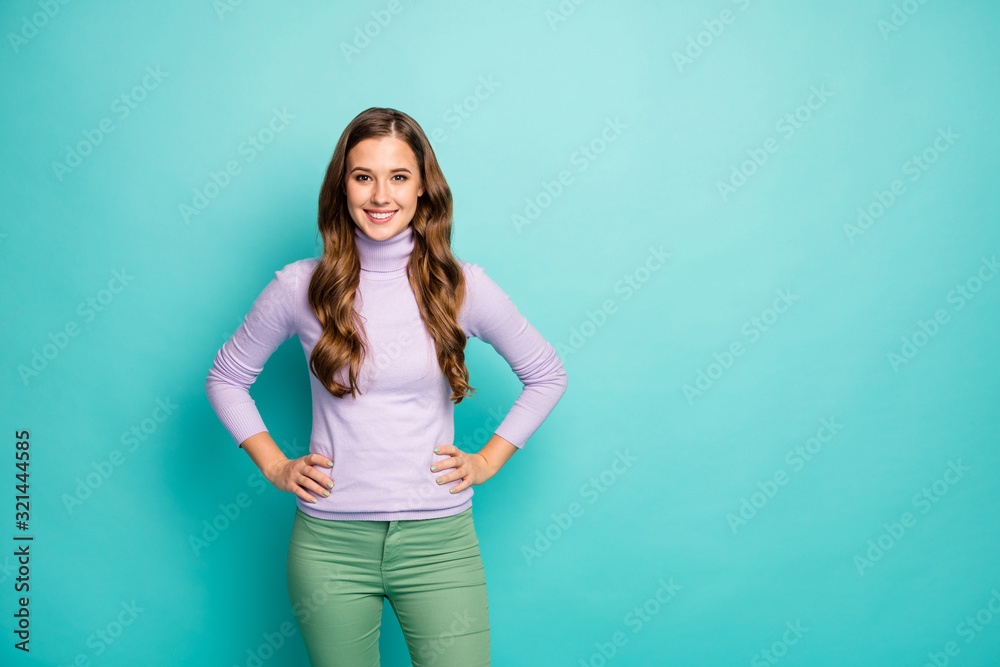 Photo of beautiful pretty lady long curly hairstyle positive good mood hands by sides wear lilac purple sweater pastel green trousers isolated blue color background