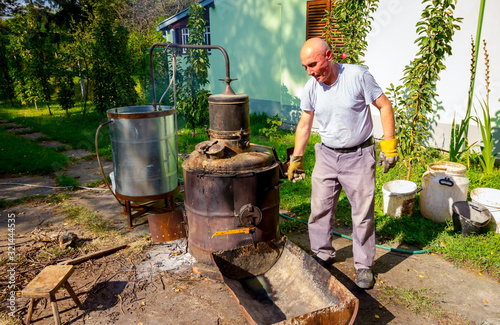 Man is manually mixing fruit marc in distillation apparatus for making domestic alcohol liquor photo