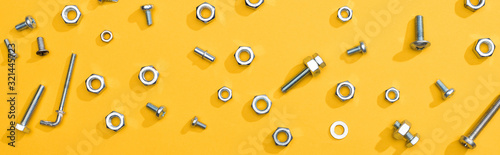 Top view of metal nuts and bolts on yellow background, panoramic shot