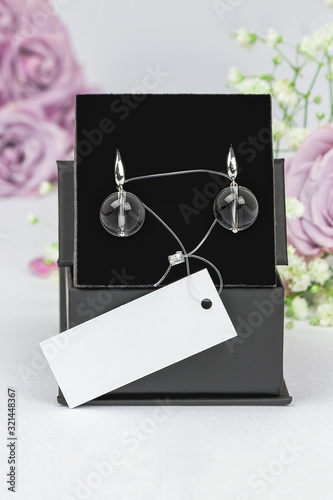 Luxury elegant earrings made of white metal (silver, platinum) with natural rock-crystal rhinestone on a velvet black pillow in a box. Beauty Accessory Brand Concept, mockup, vertical orientation