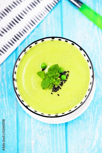 Homemade green cream soup with green peas, mint, black cumin or nigella sativa on a light blue background, top view