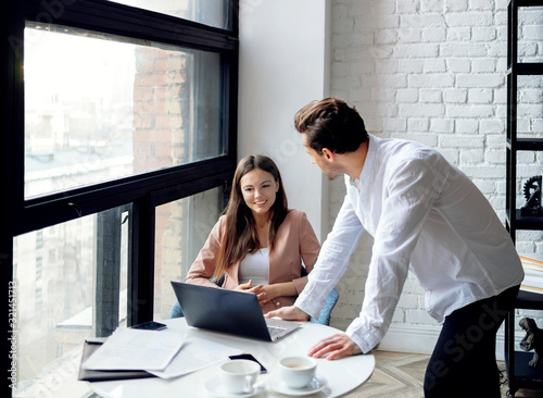 Couple of young businesspeople discussing work and project. Young businesswoman looks at her colleague and smiles.  photo