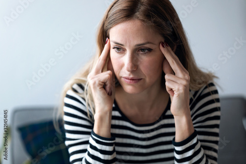Young woman with headache sitting on the sofa in the living room at home.
