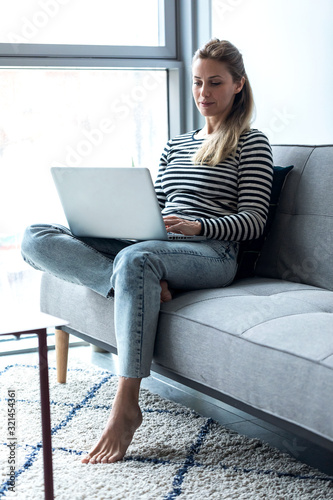 Pretty young woman using her laptop while sitting on sofa at home. Free Download Pretty young woman using her laptop while sitting on sofa at home. - GFXLoad