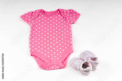 baby expectation concept with baby socks near pink bodysuit for newborn with polka dot on white