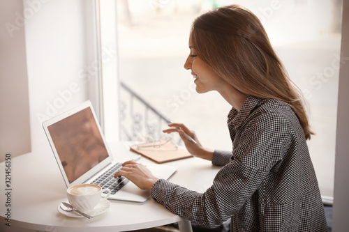 Young blogger working with laptop at table in cafe