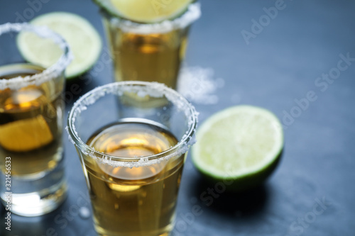Mexican Tequila shots with salt and lime slices on grey table, closeup