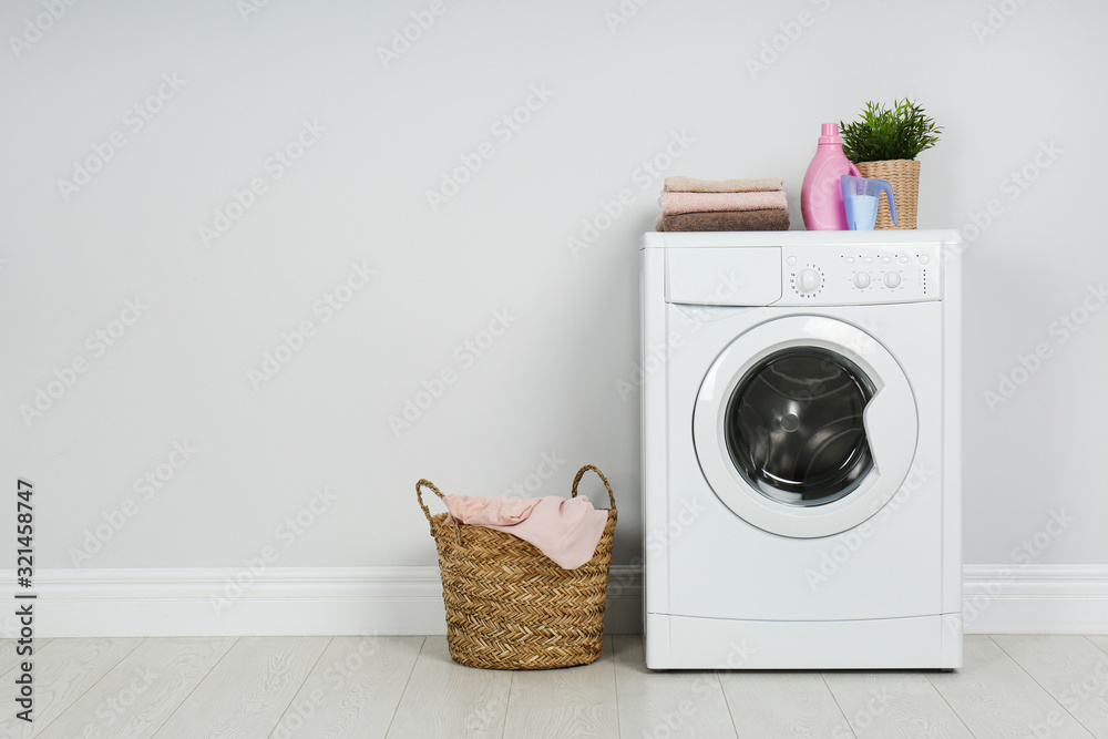 Modern washing machine with stack of towels, detergents and laundry basket  near white wall. Space for text Stock Photo | Adobe Stock