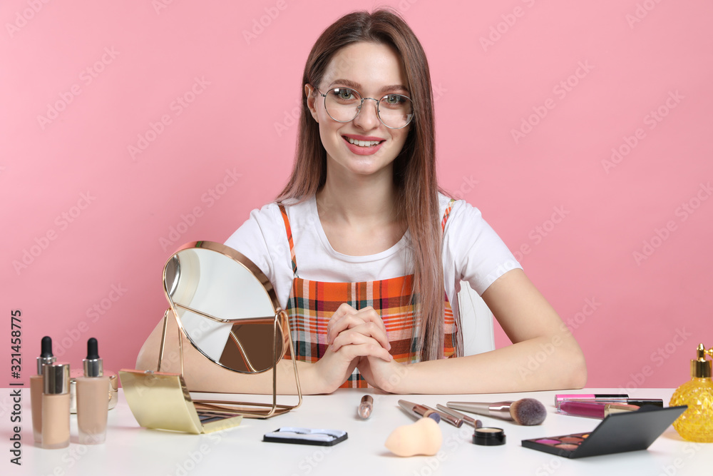 Beauty blogger at table with different cosmetic products against pink background Beauty blogger at table with different cosmetic products against pink background