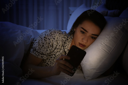 Foto Young woman addicted to smartphone in bed at night
