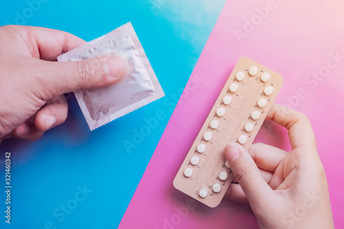 Man and woman hands are hording contraception pills and condom on blue and pink background. Male and female contraceptives concept. Bitrh control concept.
