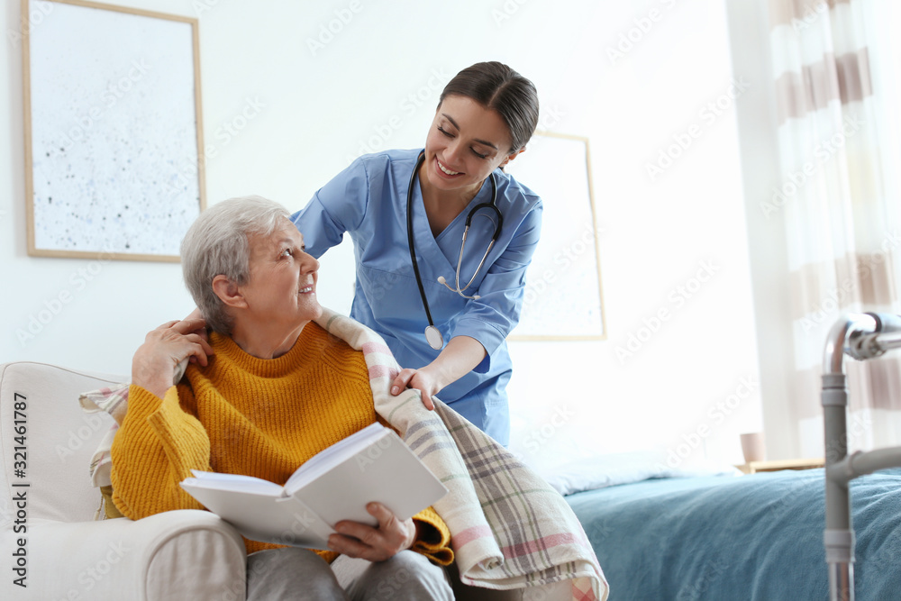 Fototapeta premium Care worker covering elderly woman with plaid in geriatric hospice