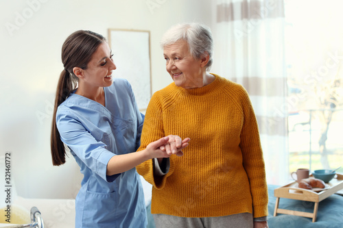Fototapeta Care worker helping elderly woman to walk in geriatric hospice