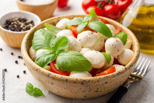 Traditional Italian caprese salad with mozzarella cheese, cherry tomatoes and basil in ceramic bowl on concrete background. Selective focus.