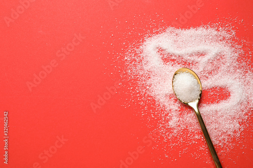 Granulated sugar and spoon on red background, flat lay. Space for text photo