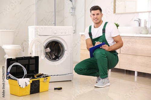 Repairman with clipboard and toolbox near washing machine in bathroom