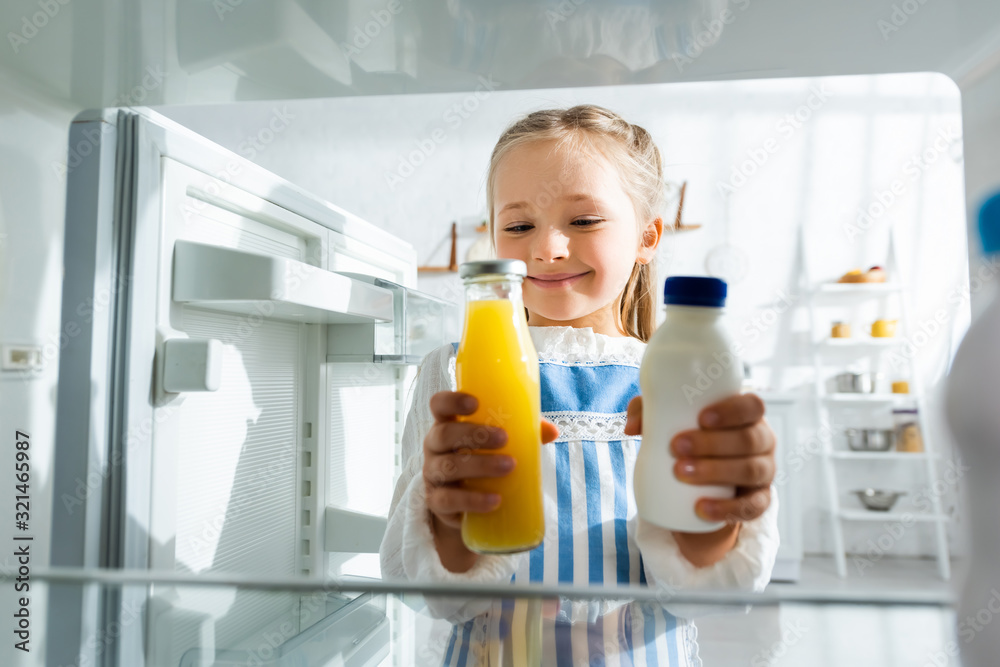 selective focus of smiling kid holding bottles with orange juice and milk