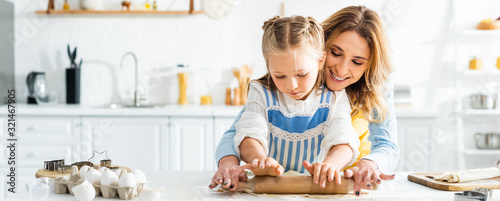 panoramic shot of smiling mother and cute daughter rolling dough on table