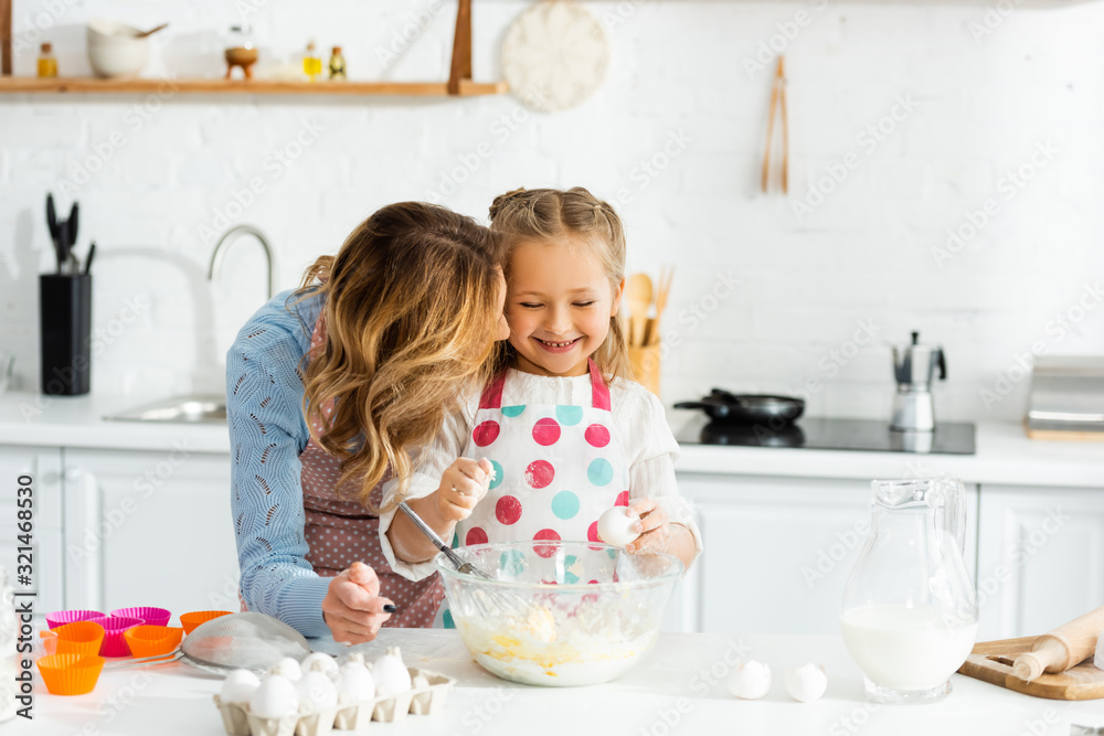 Mother and daughter smiling and happy during making dough for cupcakes together