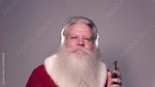 Senior Caucasian smiling man in Santa Claus suit with splendid grey hair, mustache and beard, dancing with sell phone and headgear in slow motion. Funny portrait of handsome European people on white